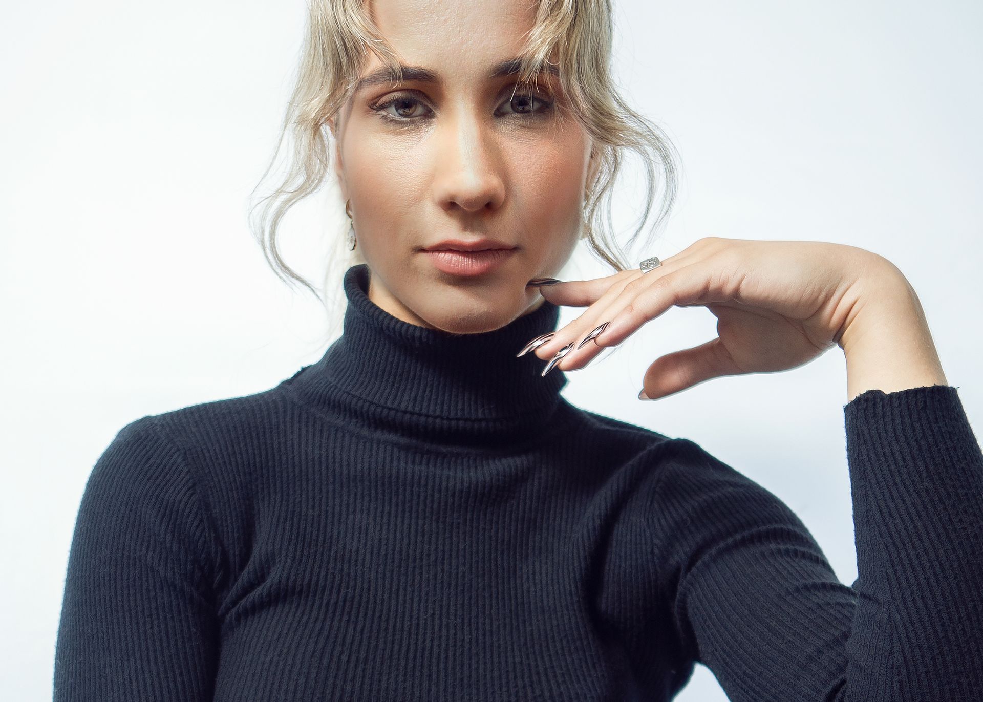 A woman wearing a black turtleneck sweater is taking a selfie with her hand on her chin.