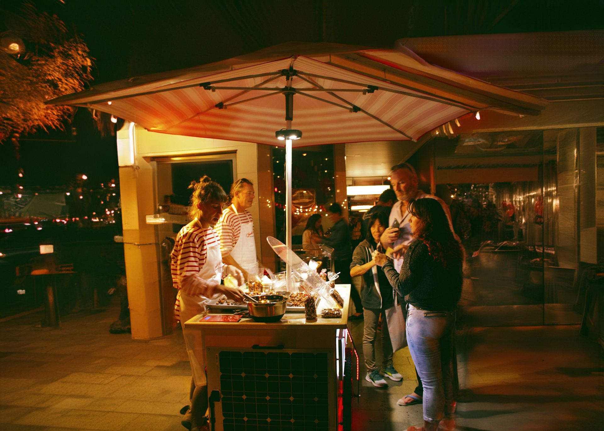 A group of people are standing around a food cart at night.