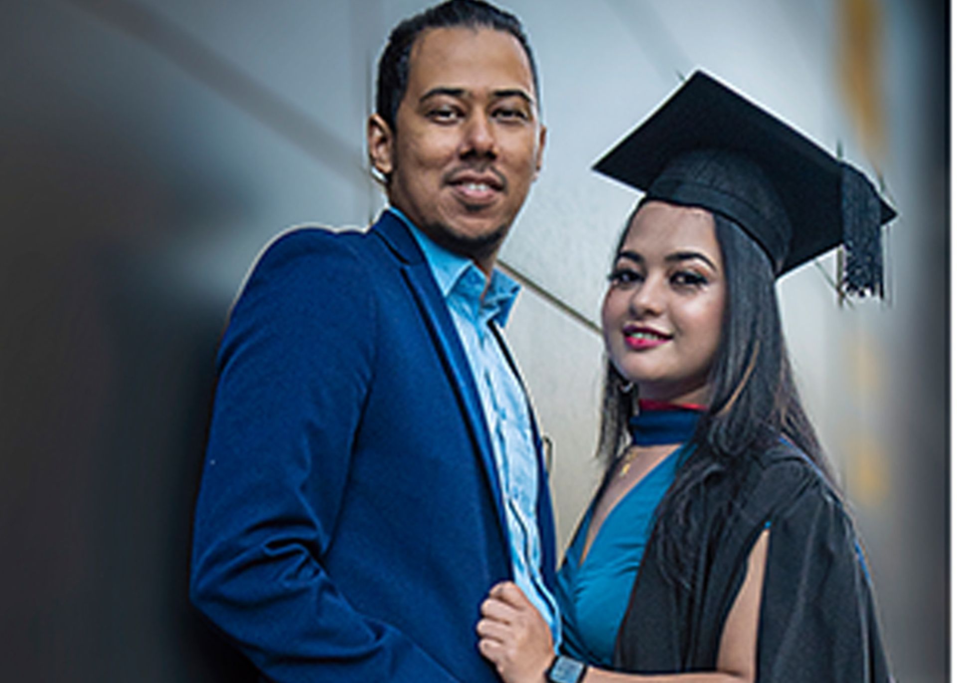 A man and a woman are posing for a picture together . the woman is wearing a graduation cap and gown.