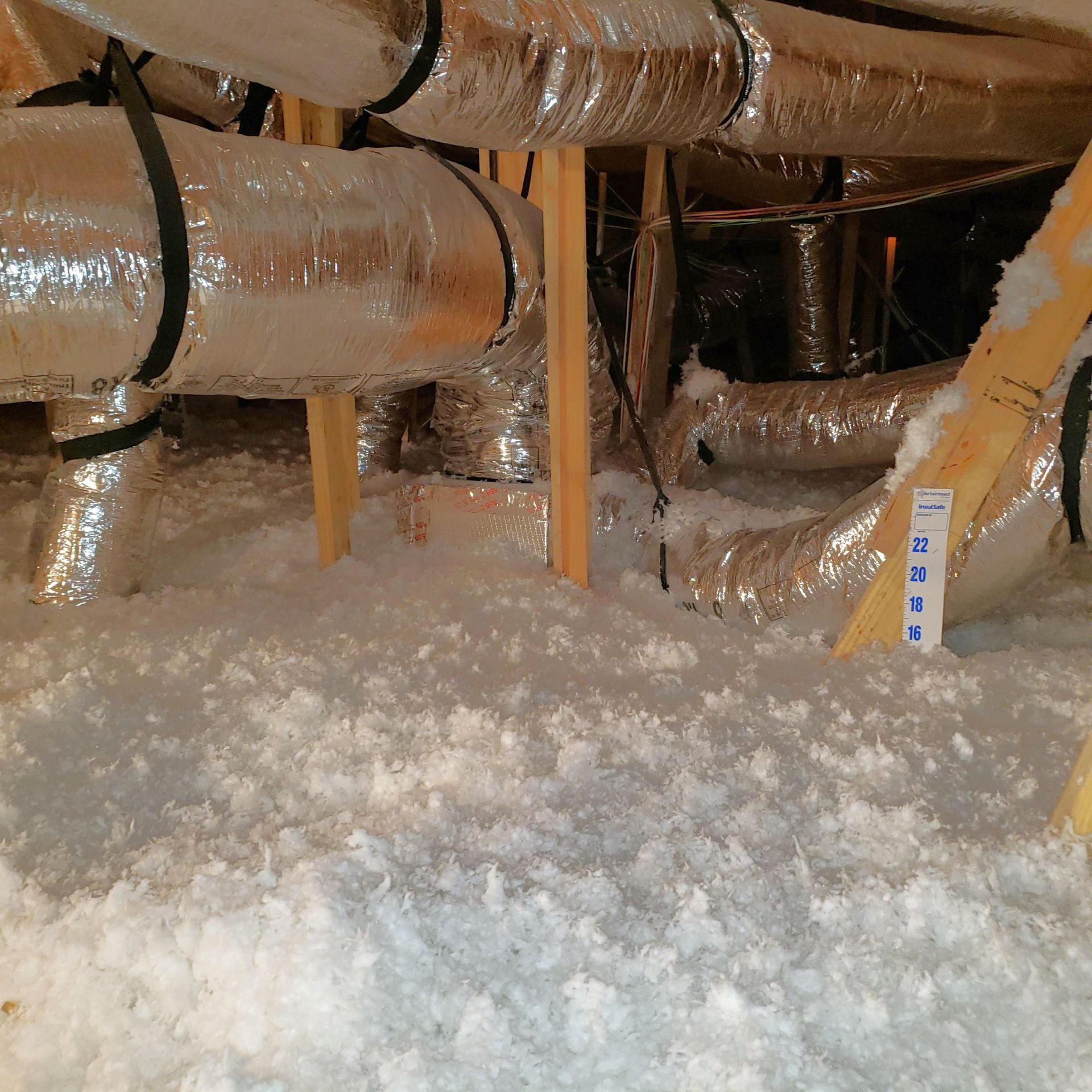 Attic with silver ductwork, wood supports, and white insulation.
