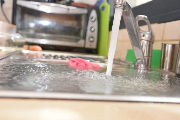 Running kitchen faucet filling a sink with water, with a toaster oven blurred in the background.