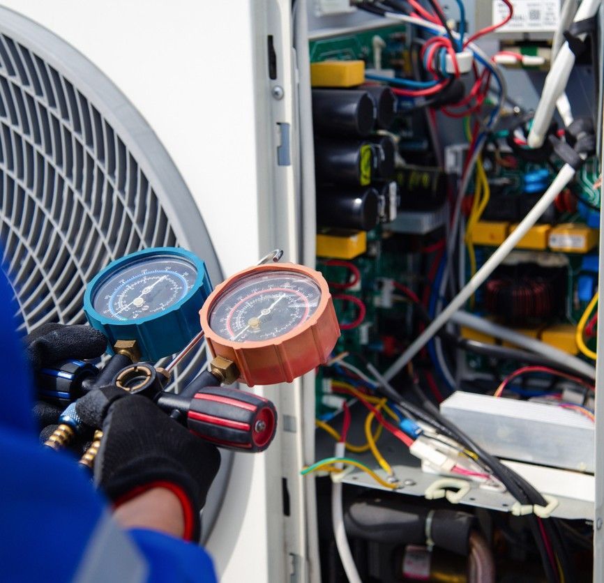 Technician using blue and orange gauges to service HVAC unit with exposed wiring
