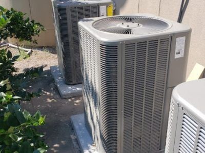 Outdoor HVAC units beside a beige wall, with one large gray air conditioner in the foreground