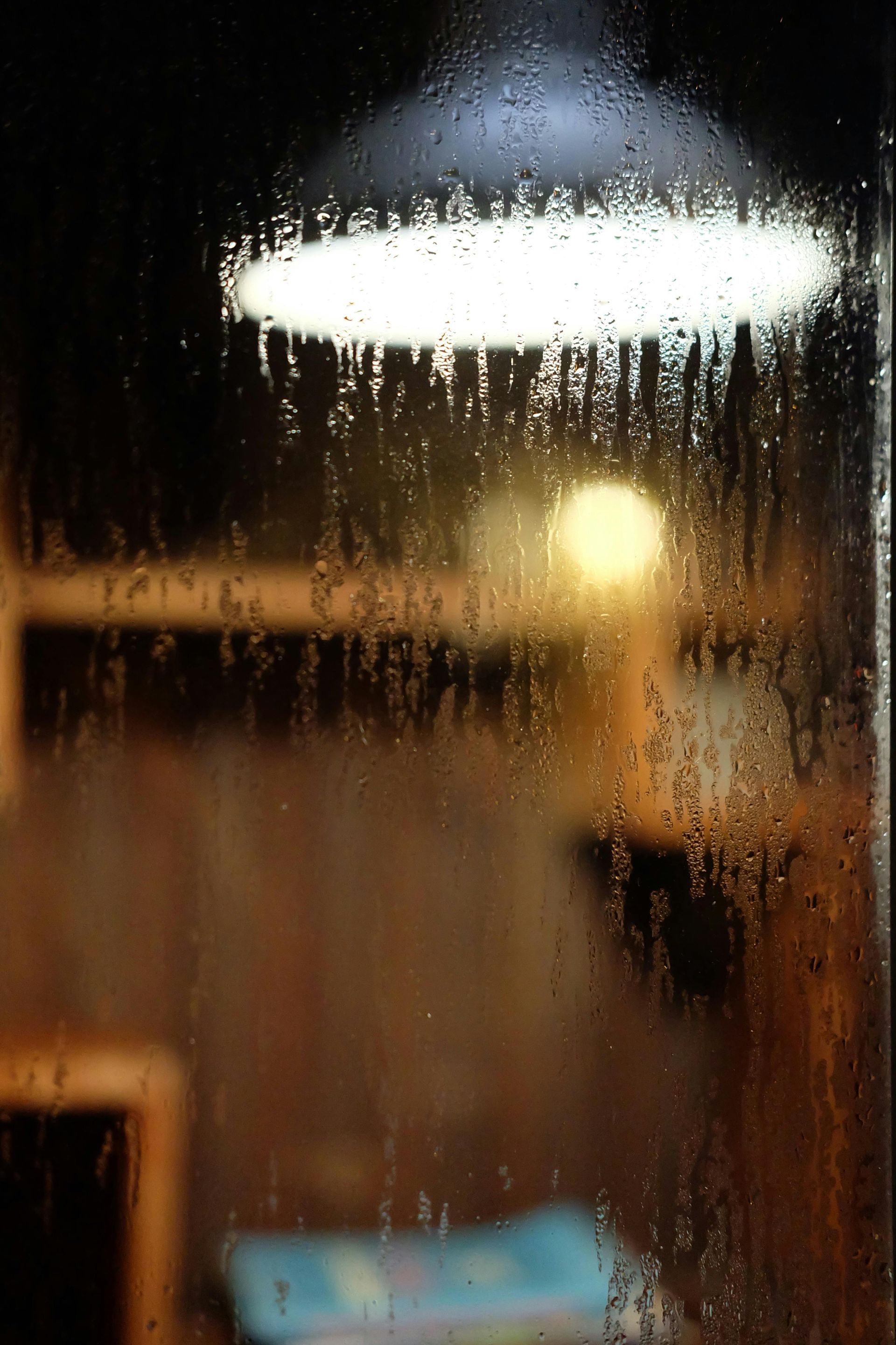 Blurred rainy window with glowing lights and a blue object at the bottom
