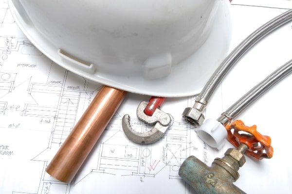 Plumbing tools and fittings with a white hard hat on blueprints