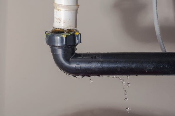 Leaking black pipe joint with water dripping from a white vertical pipe connection