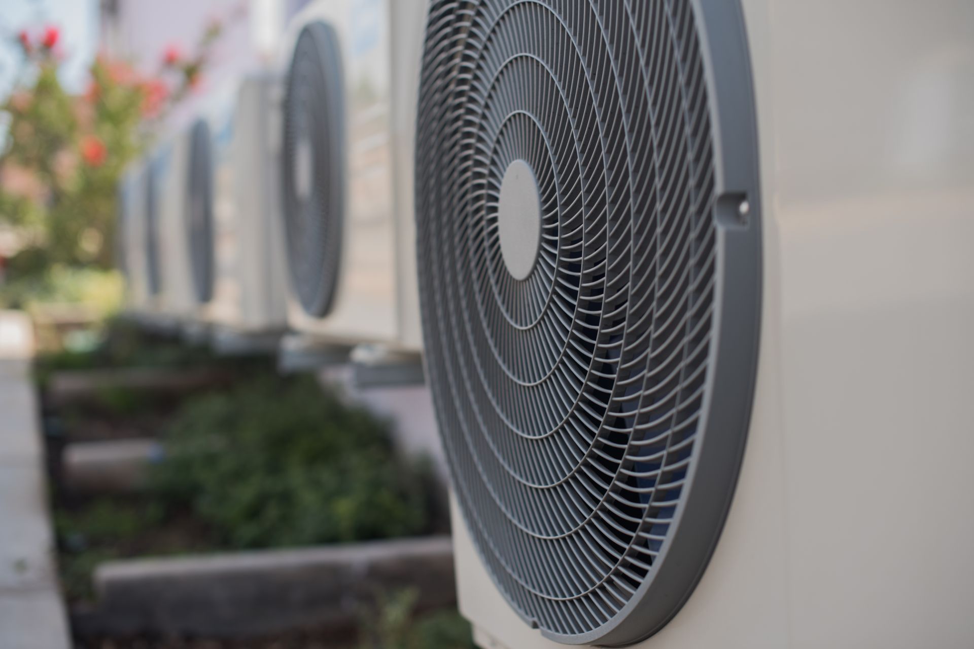 Row of outdoor HVAC unit fans along a building wall, with one large fan in the foreground