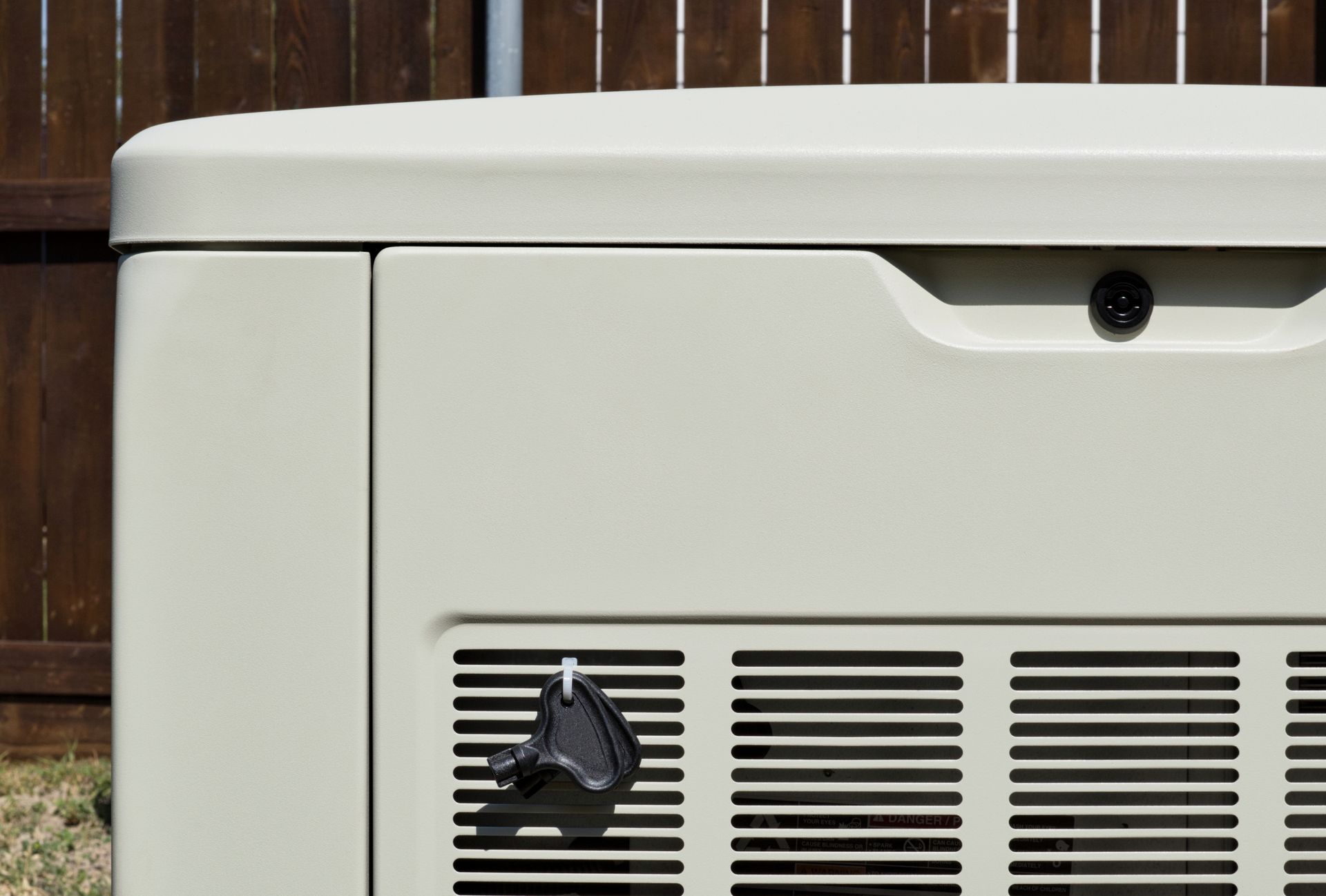 White utility box outdoors against a wooden fence, with vents and a black handle on the front.