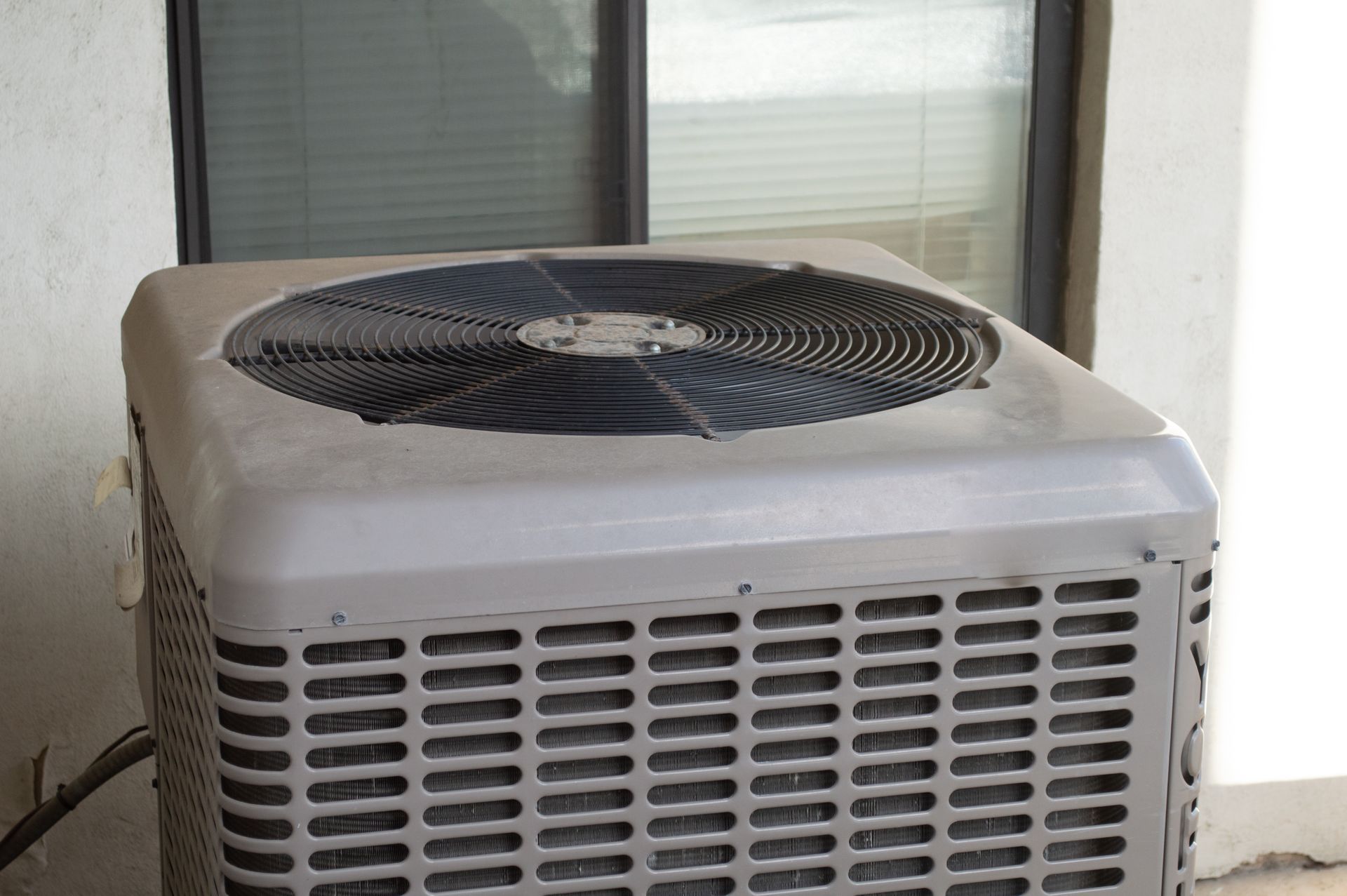Outdoor air conditioning unit with a large top fan beside a window