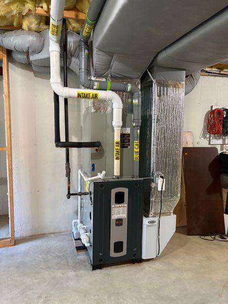 Furnace unit with ductwork in a basement setting. Pipes are white and black. Ductwork is silver.