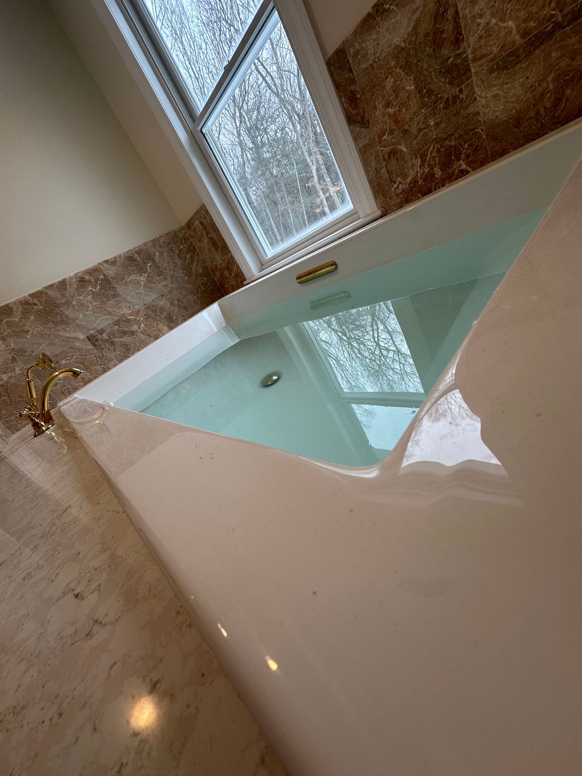 Bathtub filled with water, beneath a window. Marble wall and white trim.