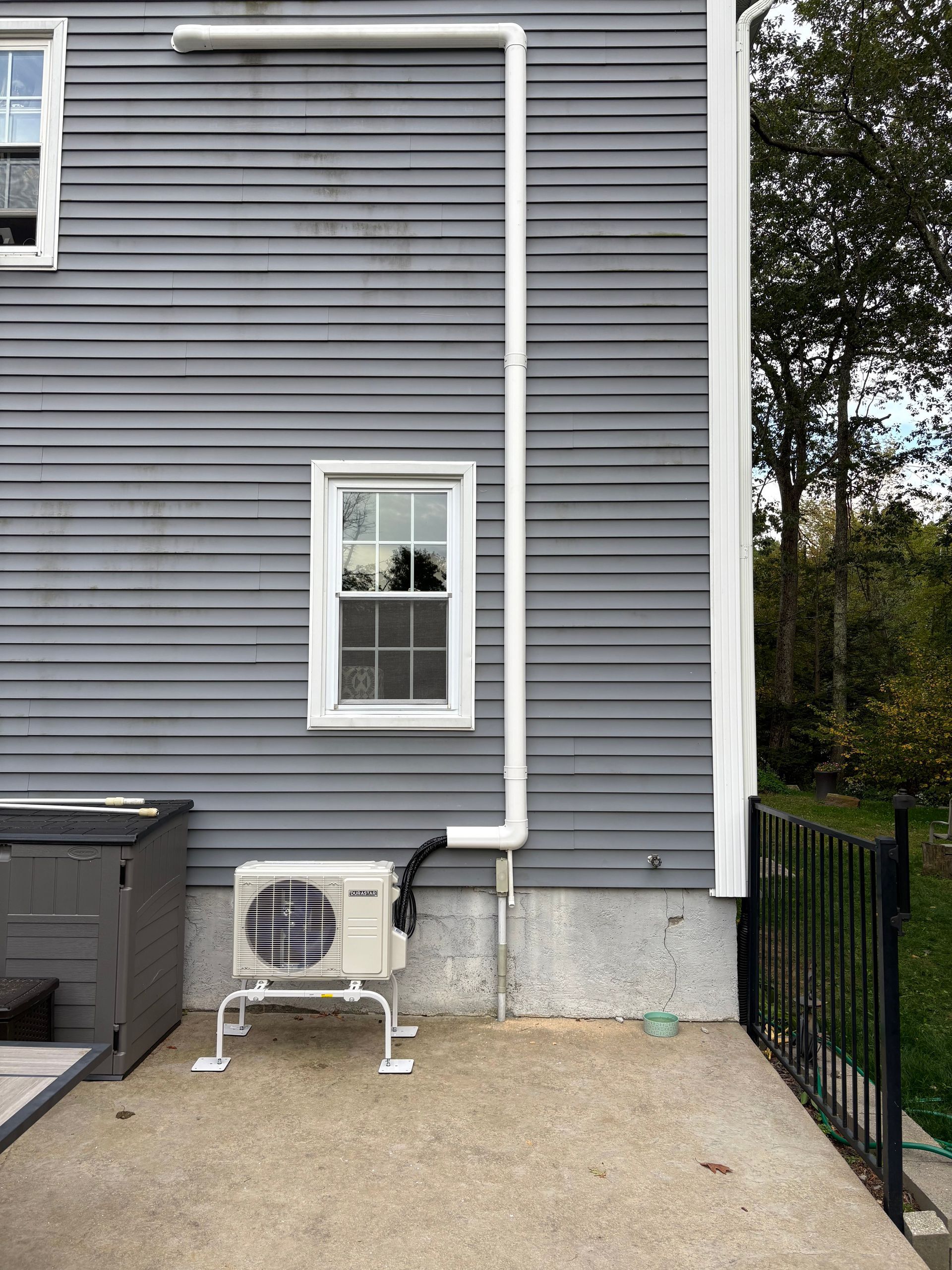 Gray house exterior with window and an outdoor AC unit; white drainage pipe.
