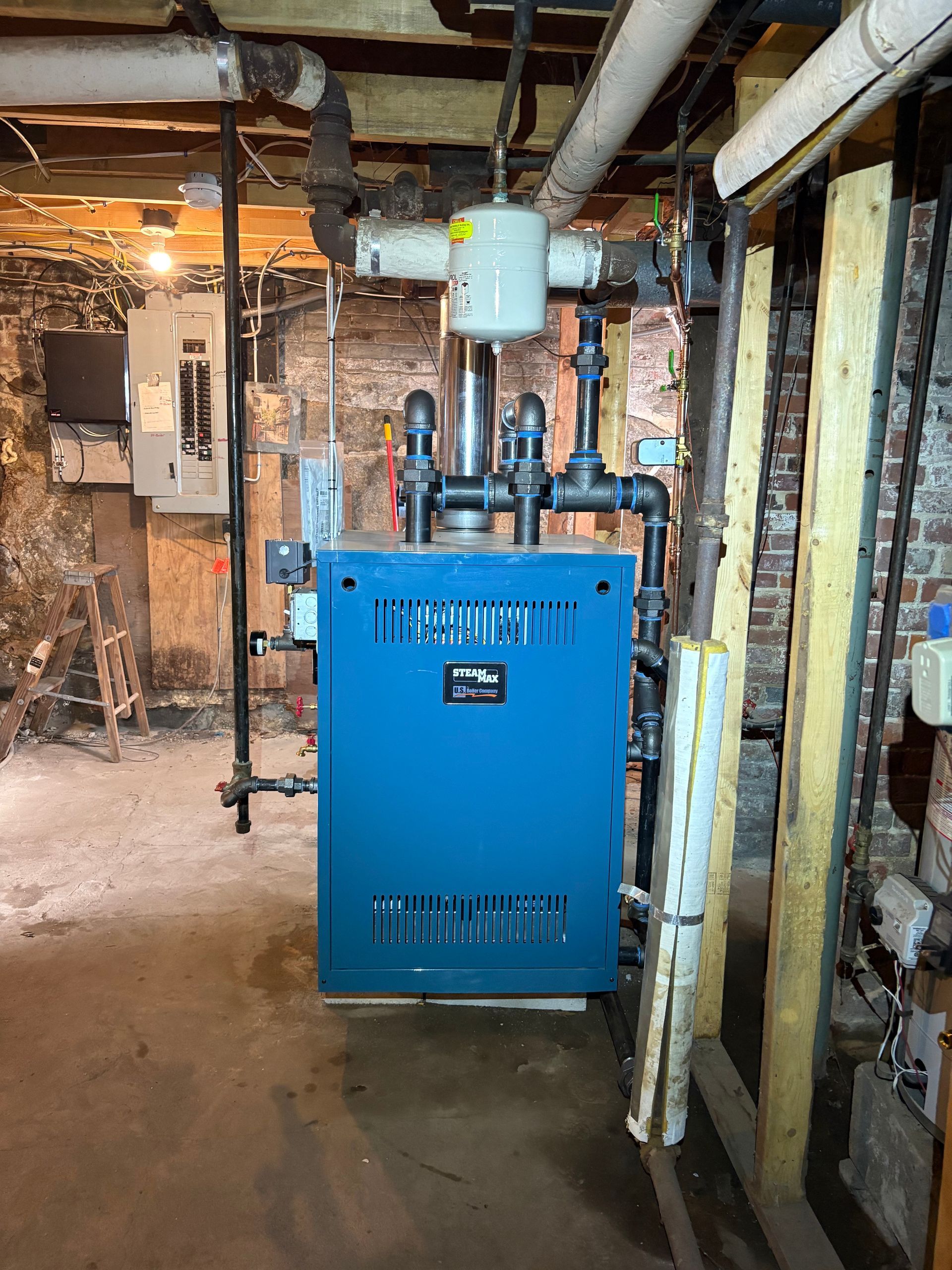 Blue boiler in a basement with pipes and electrical panel.