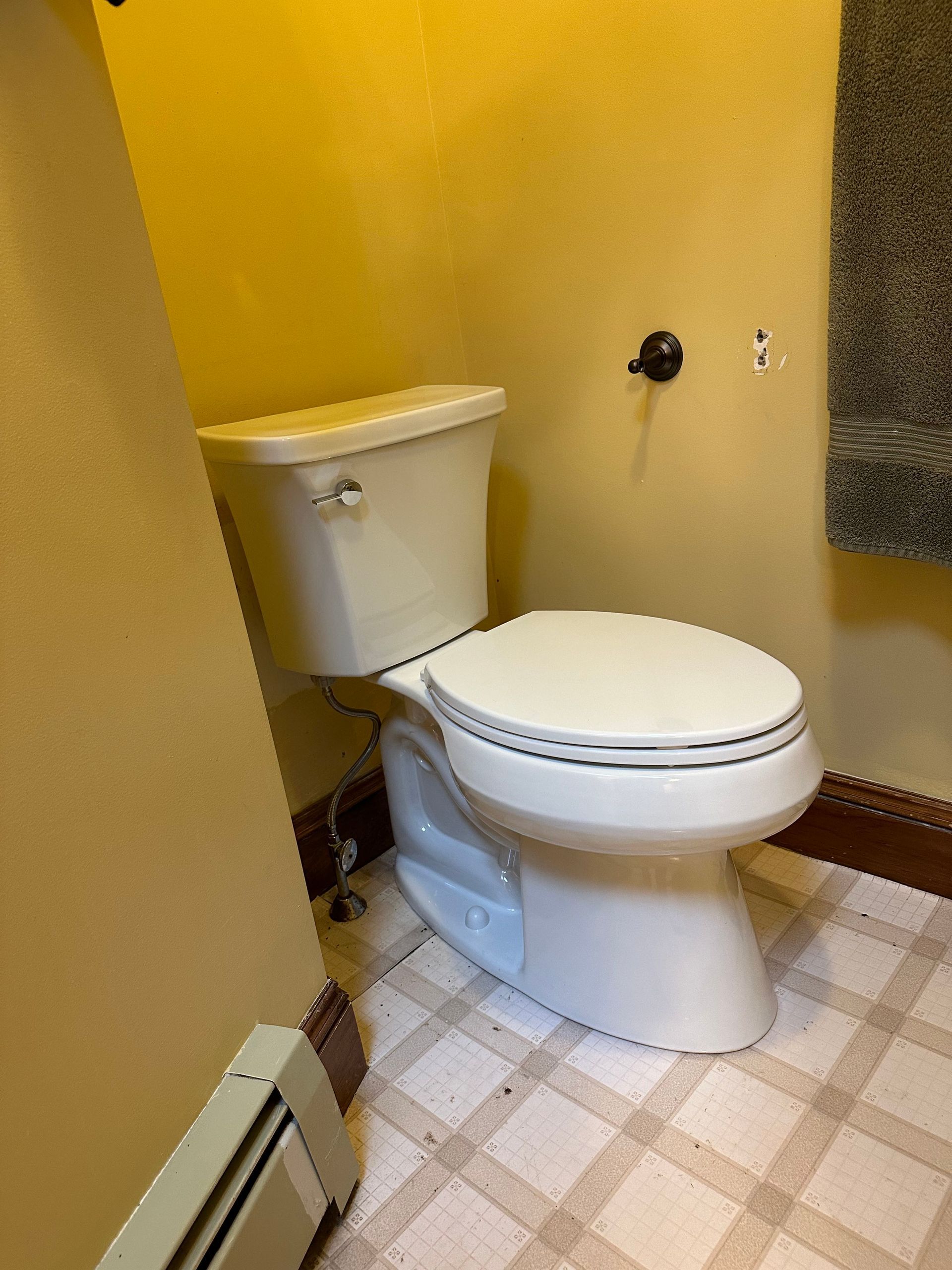 Toilet in bathroom with yellow walls, towel, and patterned floor.