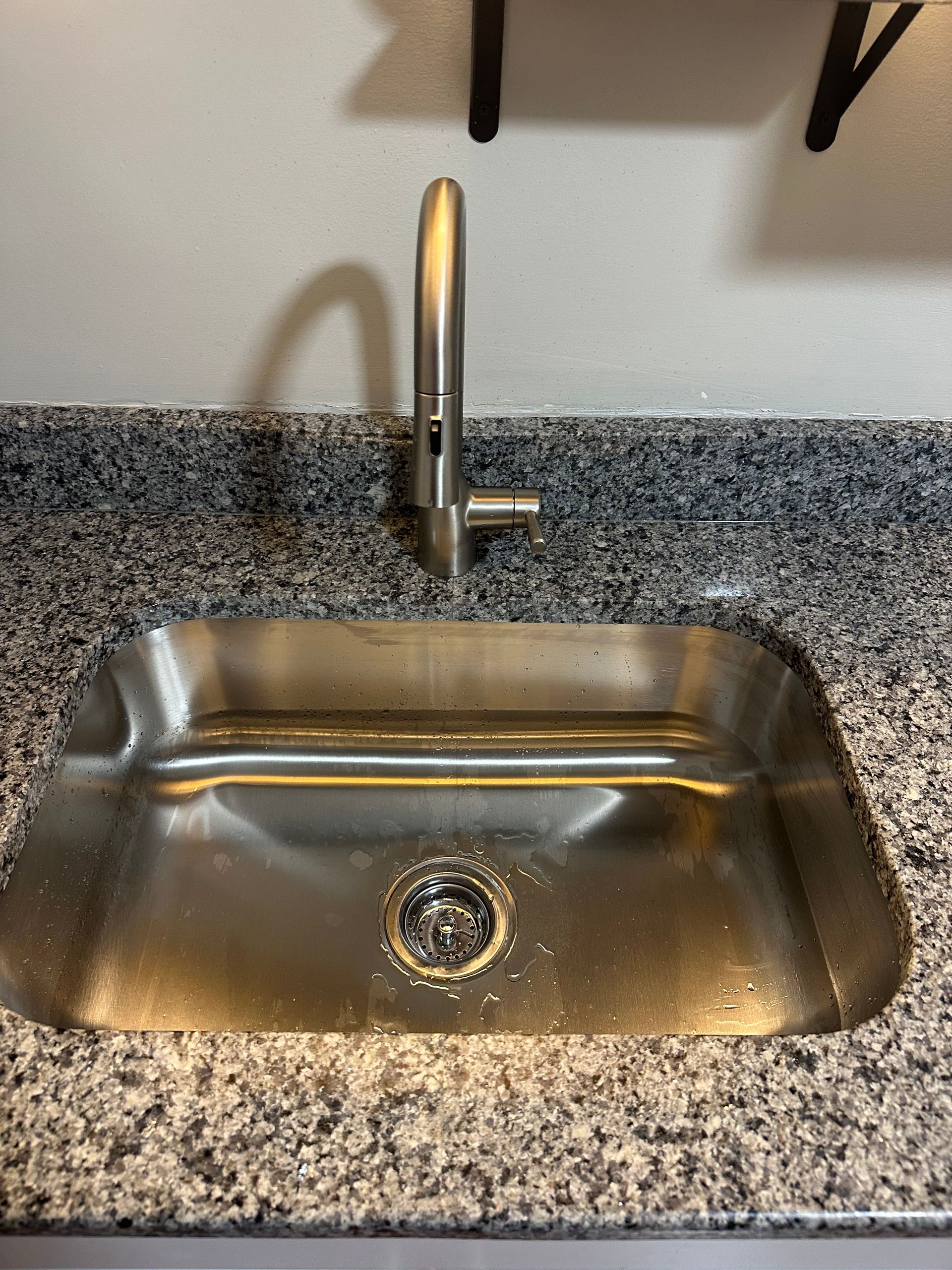 Stainless steel kitchen sink with faucet on granite countertop.