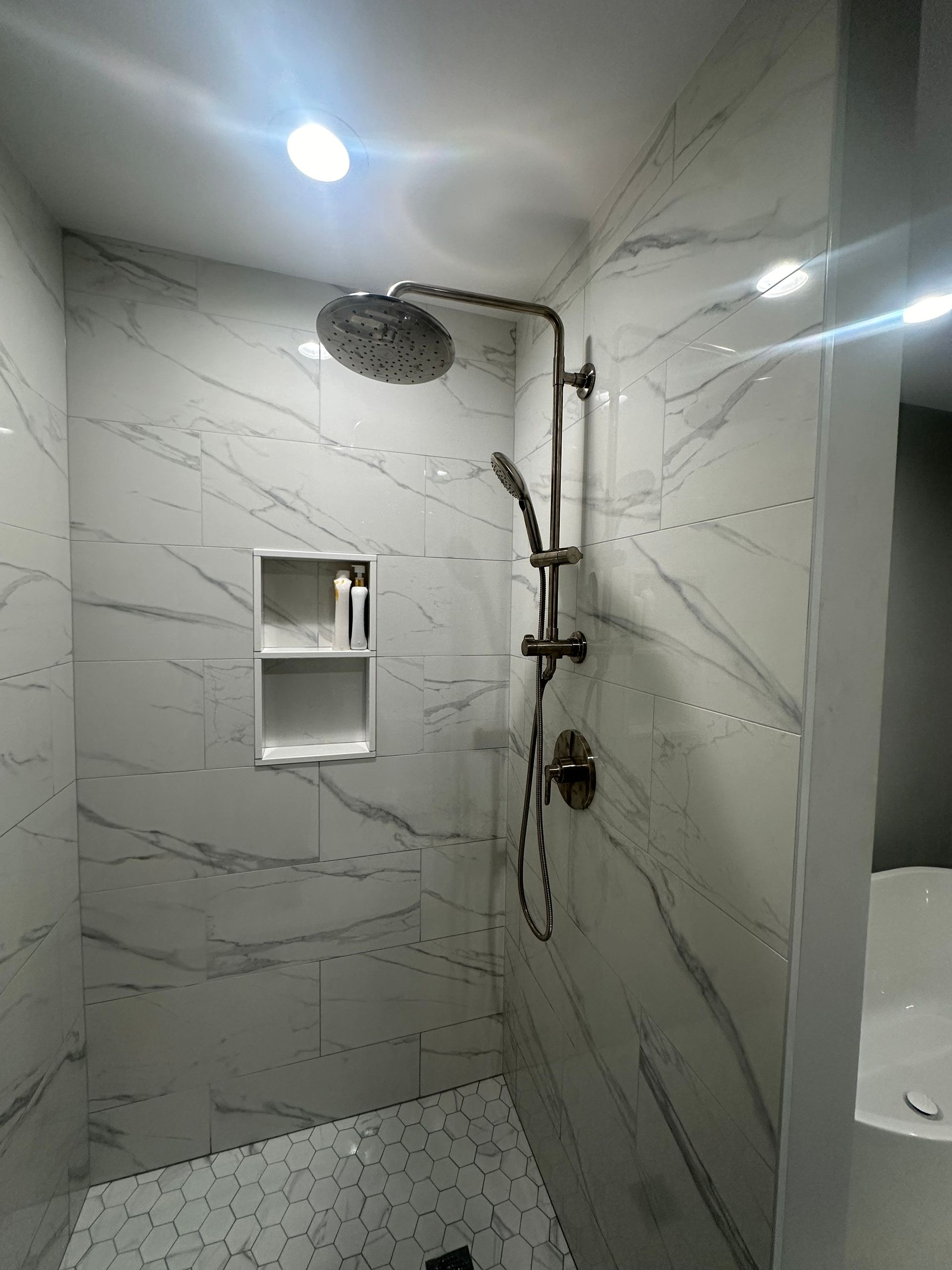 Modern shower with white marble-look tiles, a rain showerhead, and a built-in shelf.