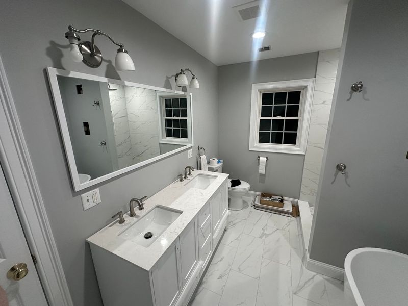 Bathroom with a white vanity, marble floor, and gray walls, featuring a large mirror and window.