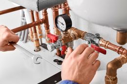 Plumber using wrench on copper pipes with a pressure gauge and valves.