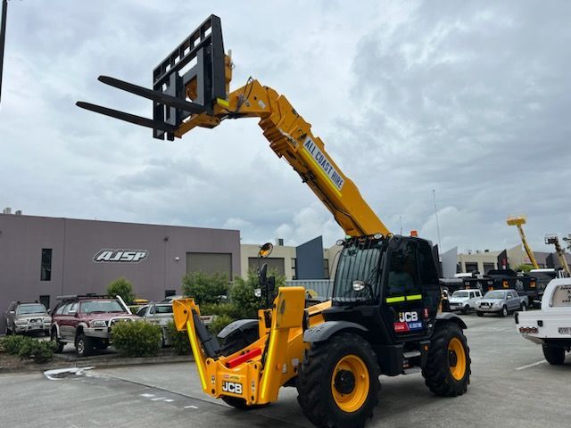 A yellow JCB telescopic handler with forks raised, parked in a paved lot outside a commercial building.