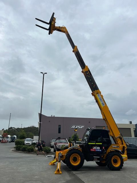 A yellow JCB telescopic handler forklift with its long boom extended upwards, parked in an outdoor lot.