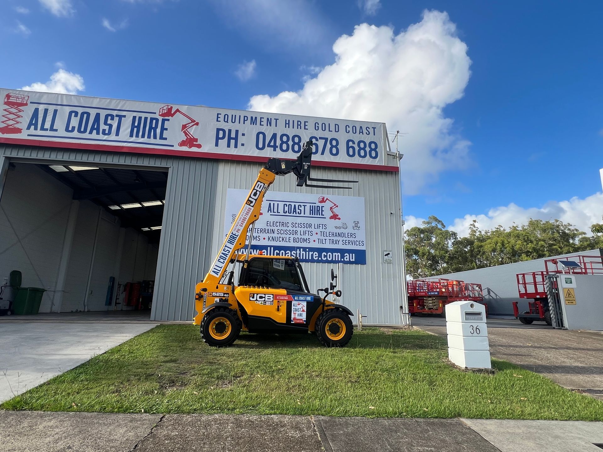 A yellow telescopic handler parked on a patch of grass in front of an 