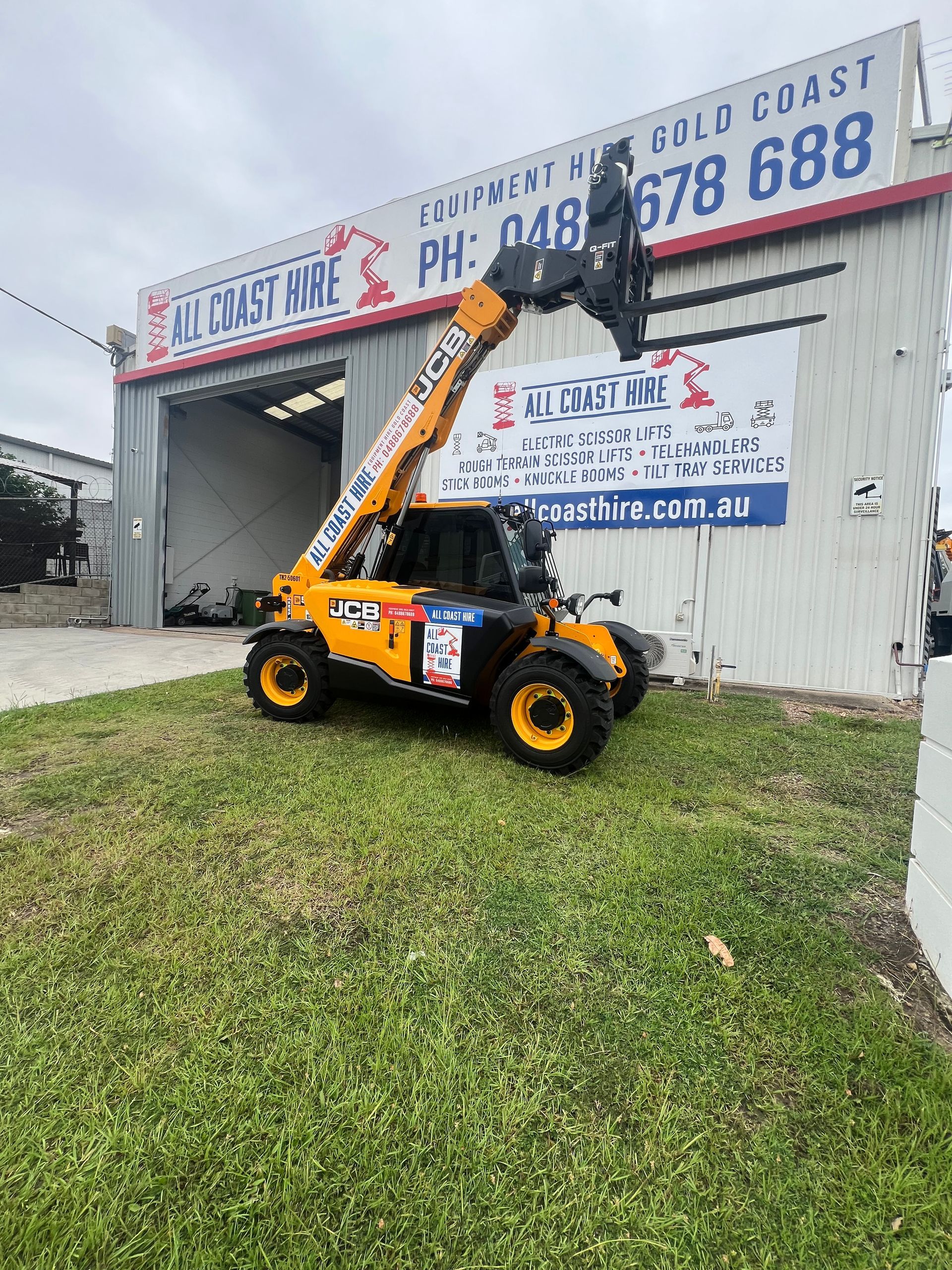 Yellow and black JCB telehandler parked on grass in front of an All Coast Hire building on the Gold Coast.