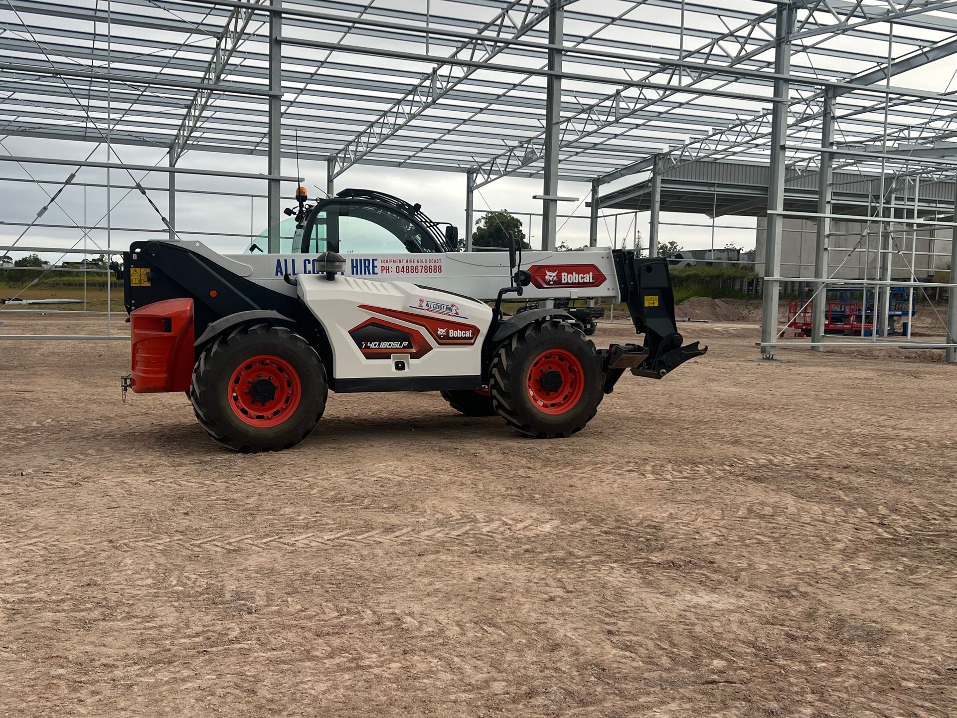 A white and red Dieci telehandler parked on a gravel construction site in front of a metal building frame.