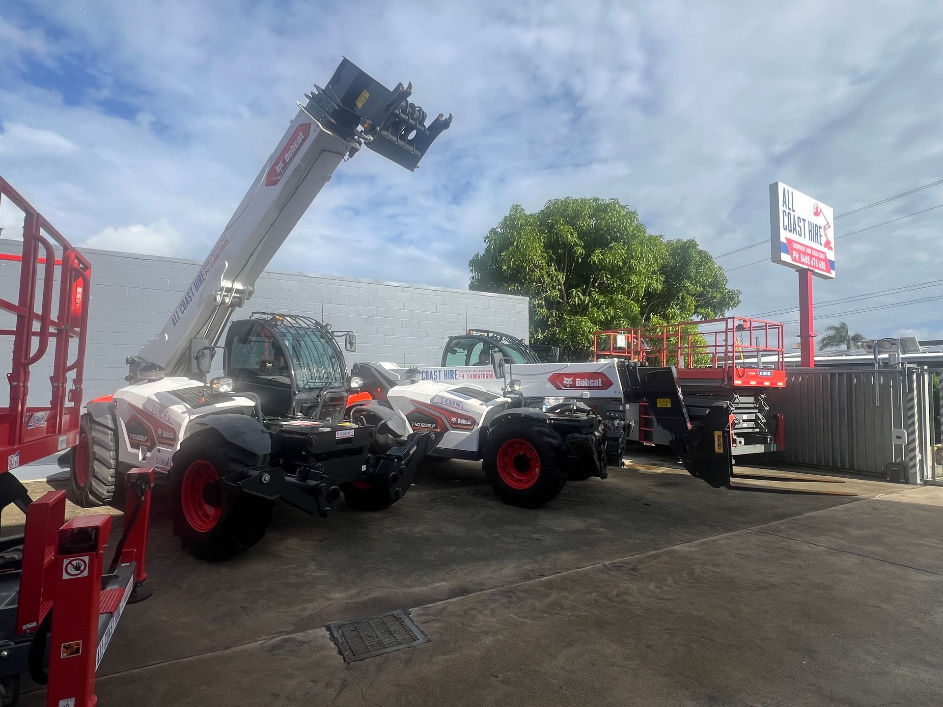 Several white and red telescopic handlers parked in an outdoor equipment lot under a blue sky.