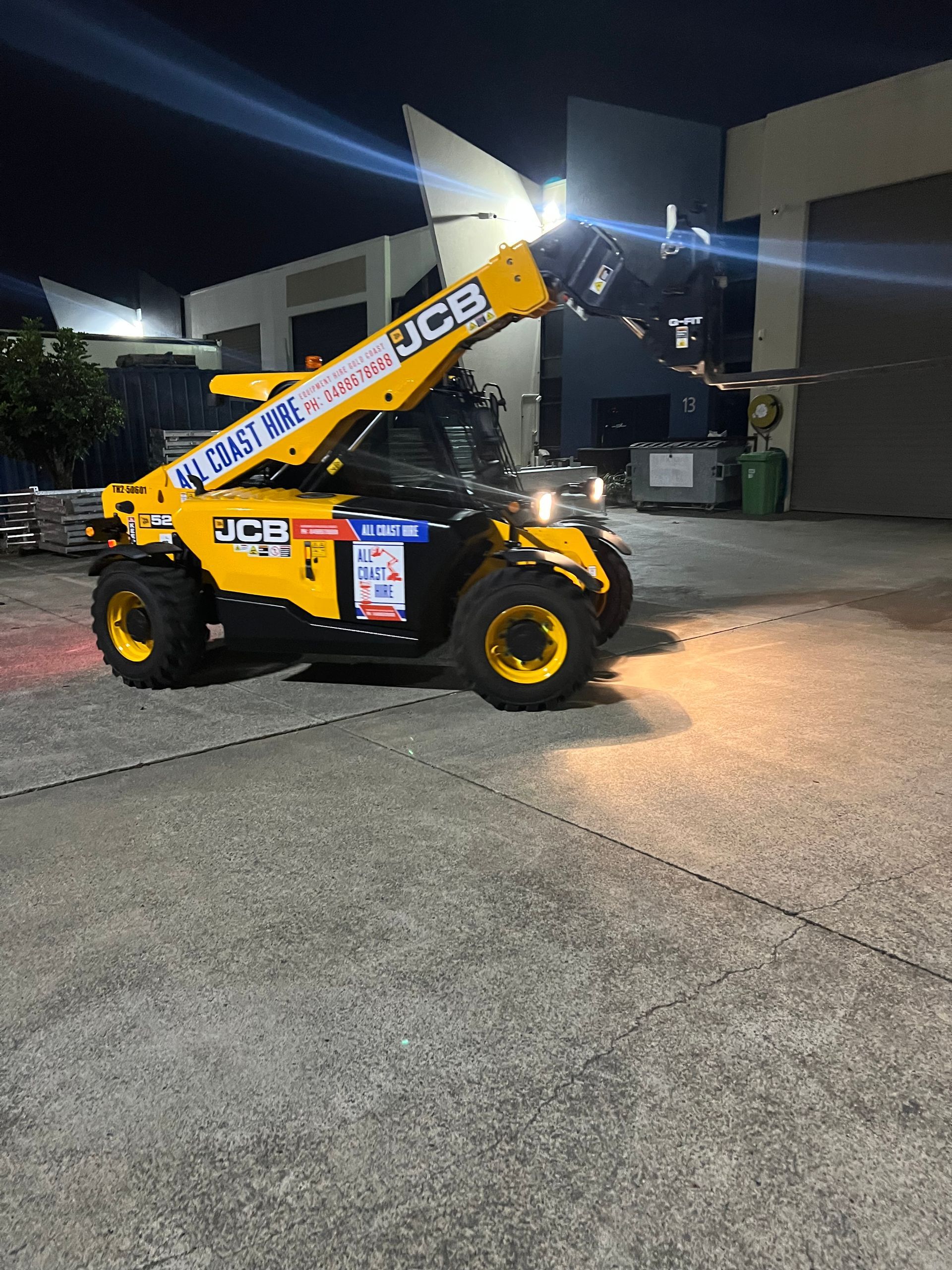 A yellow JCB telehandler parked on a concrete surface in front of a building at night.