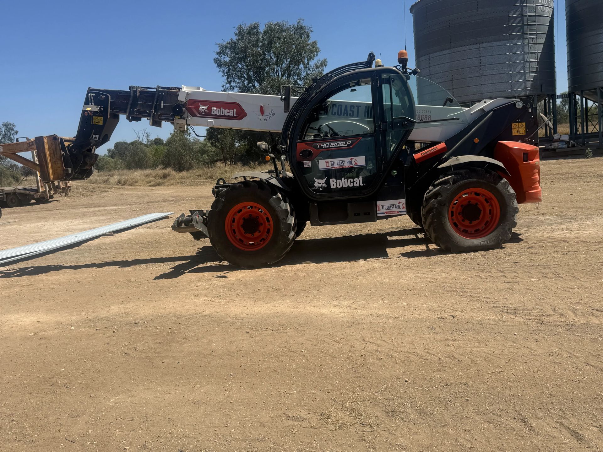 Red articulated boom lift with raised bucket beside an open warehouse in sunlight