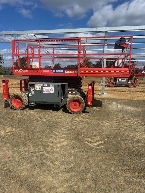 A red Skyjack scissor lift parked on a dirt construction site under a blue sky.