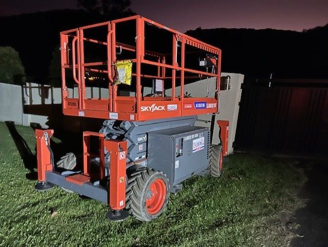 An orange and grey Skyjack scissor lift parked on a grassy area at night.