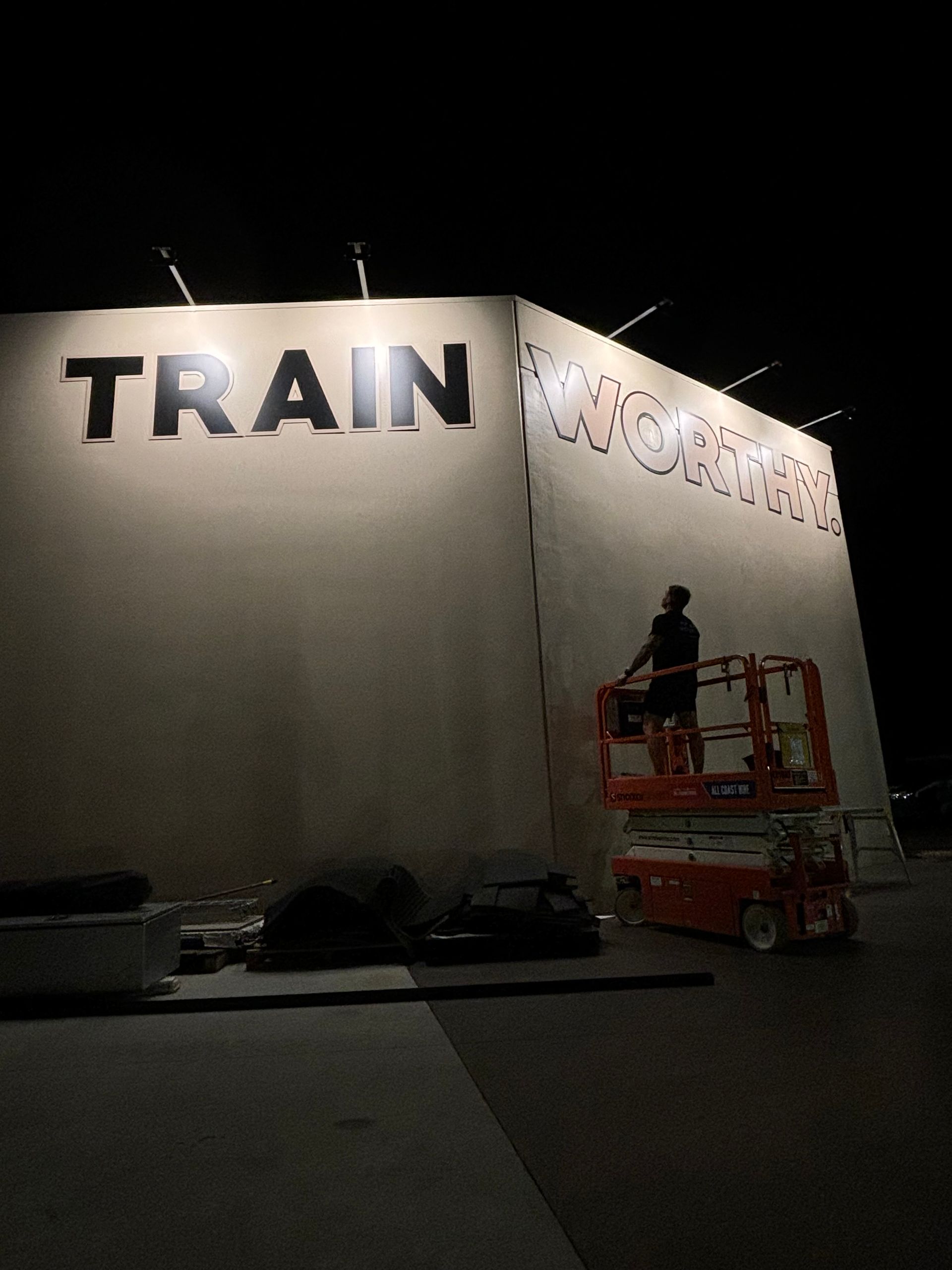 A person in a scissor lift paints the word 