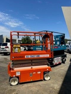 An orange Snorkel scissor lift parked next to a blue one on a sunny, paved lot.