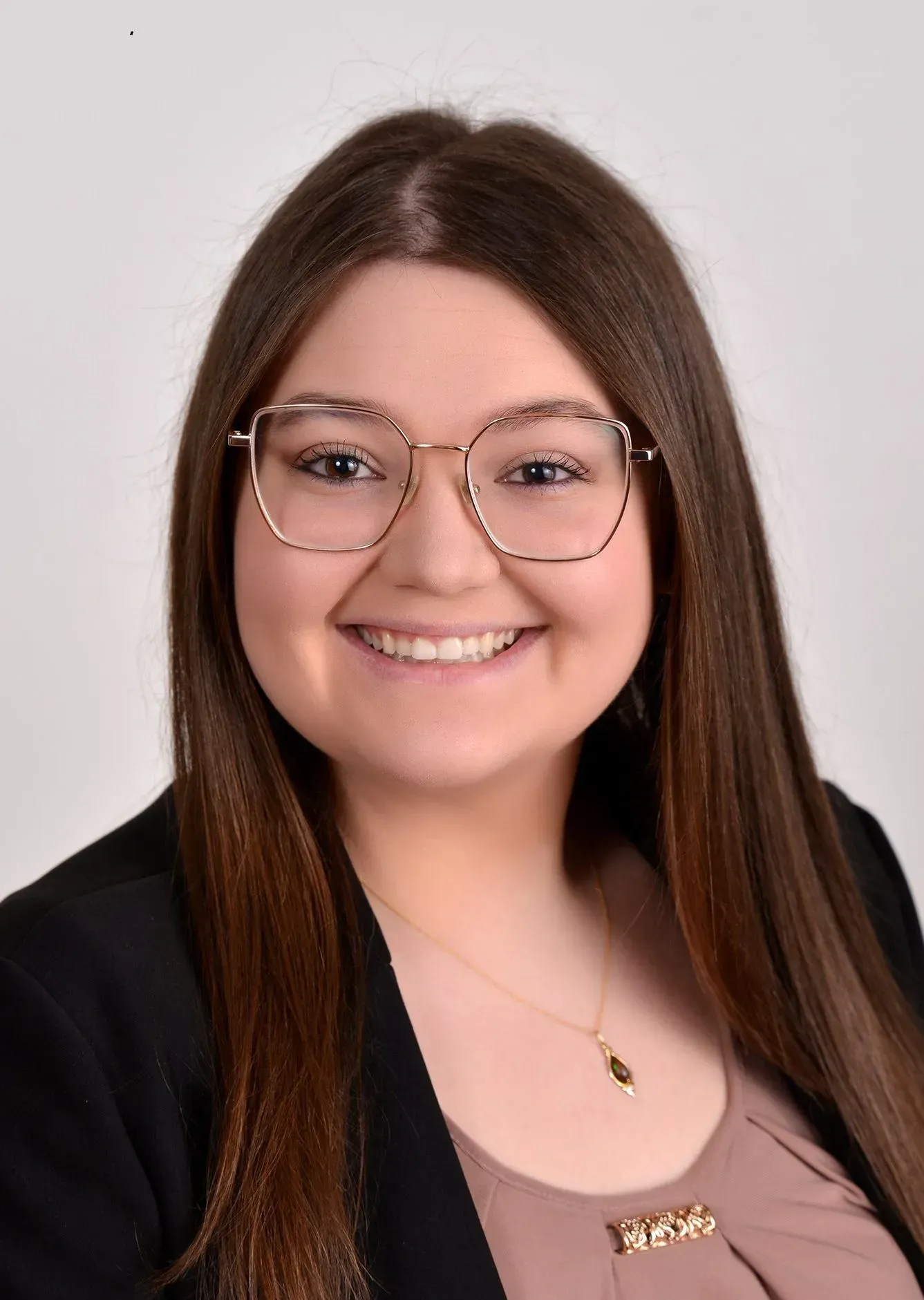 Smiling person with long brown hair and glasses against a light background