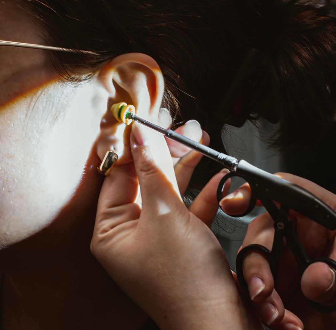 Hand adjusting a beige behind-the-ear hearing aid on a person’s ear