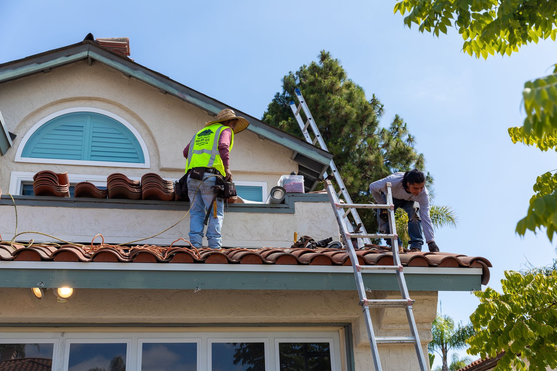 Two men are working on the roof of a house and one is wearing a yellow vest that says ' california ' on it