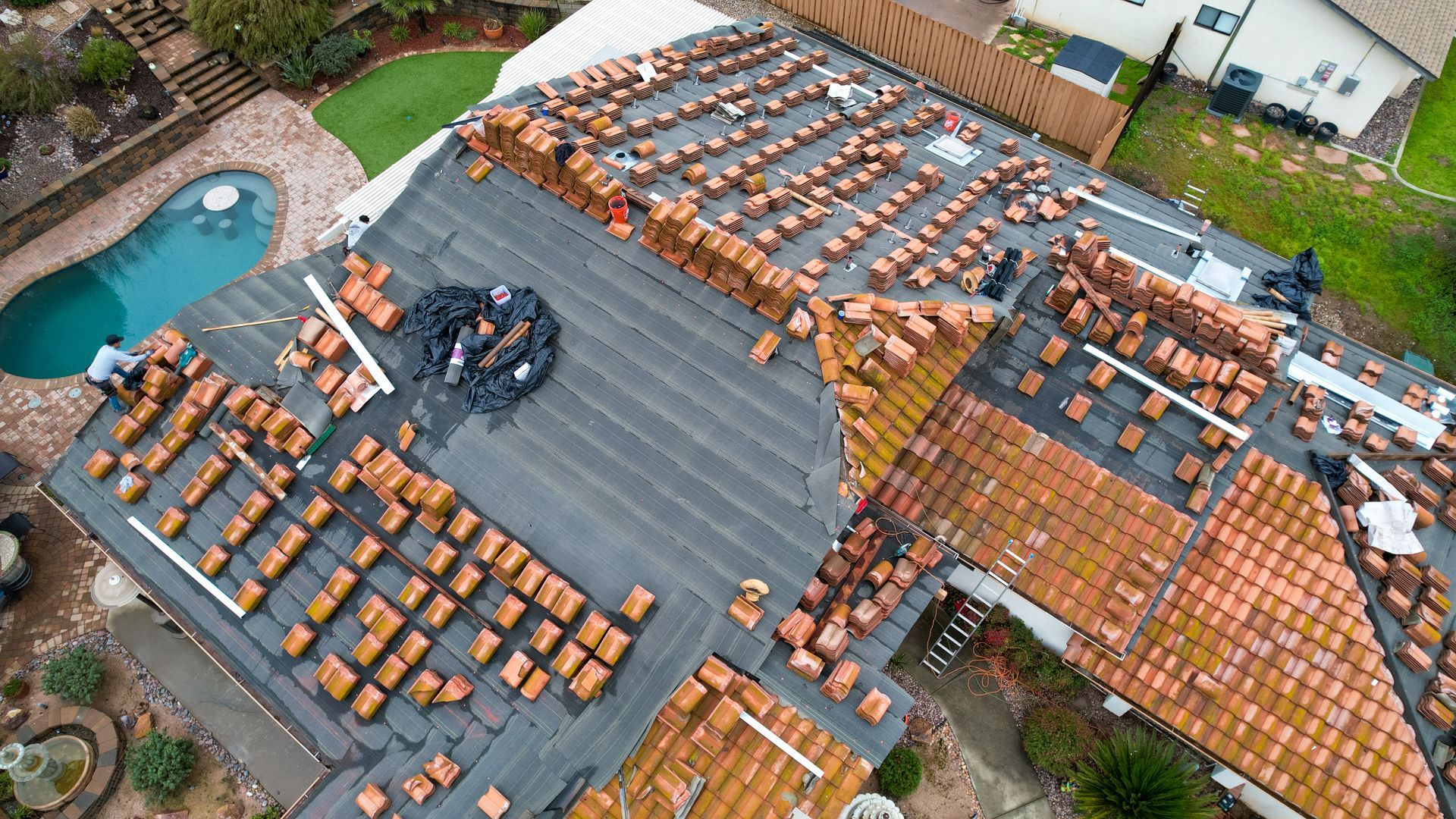 An aerial view of a roof being repaired with a pool in the background.