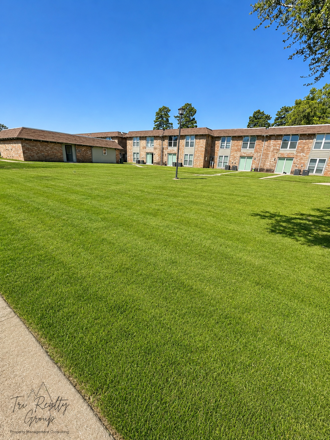 Brick apartment building behind a large green lawn under a clear blue sky
