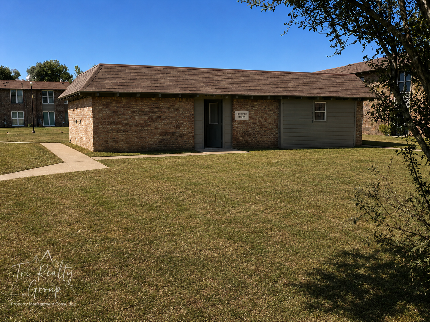 Single-story brick house with a large grassy yard and a concrete walkway under a clear sky