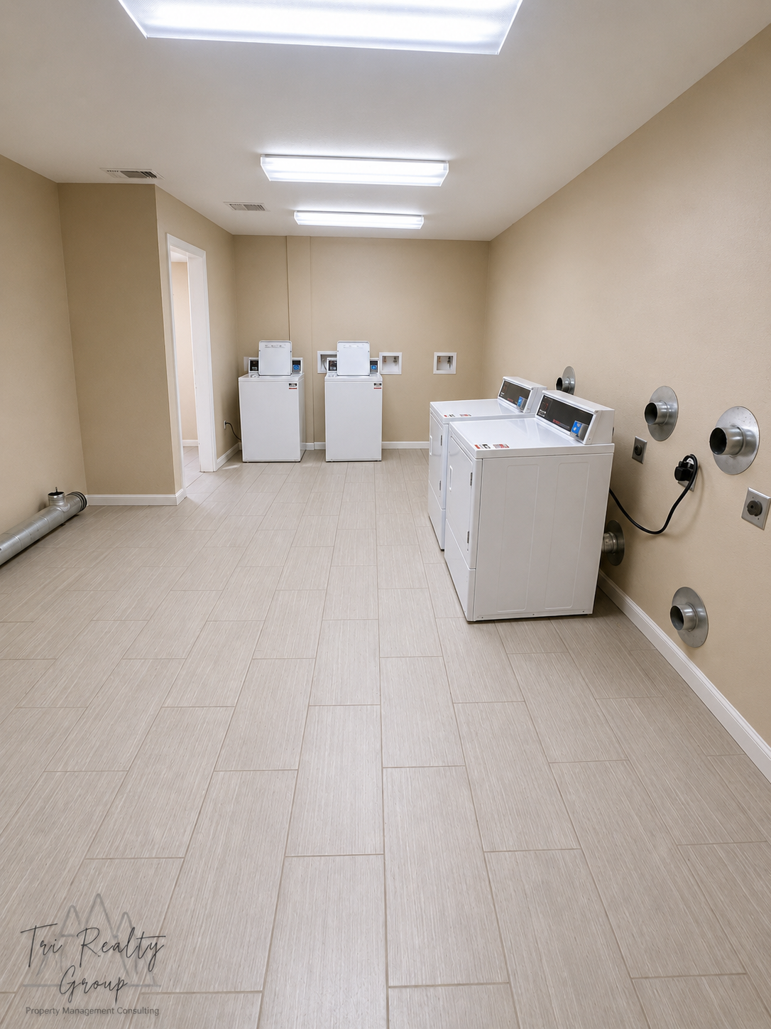 Empty laundromat with washers and dryers along beige walls and white tile floor