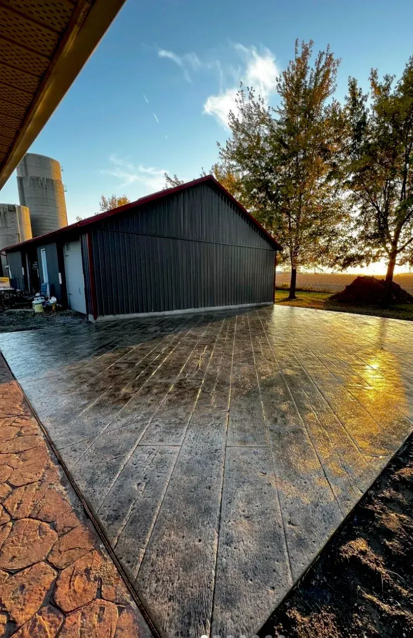 A new stamped concrete patio with a dark, patterned finish sits next to a metal shed at sunset.