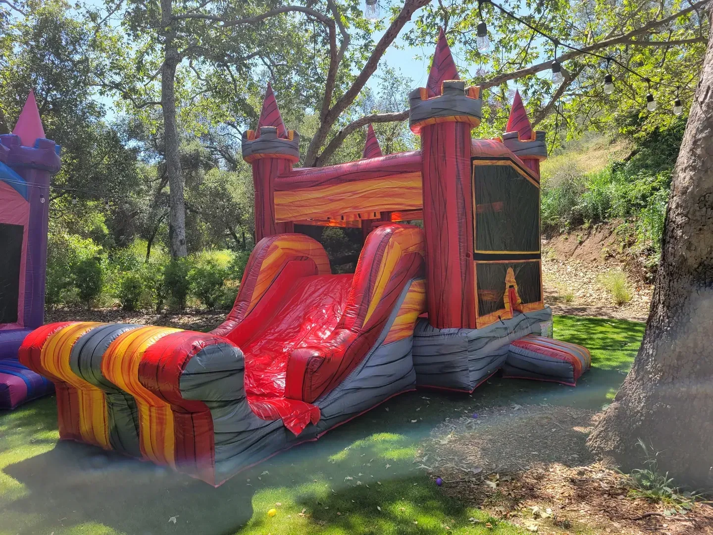 Colorful inflatable castle with a rainbow slide in a wooded outdoor setting