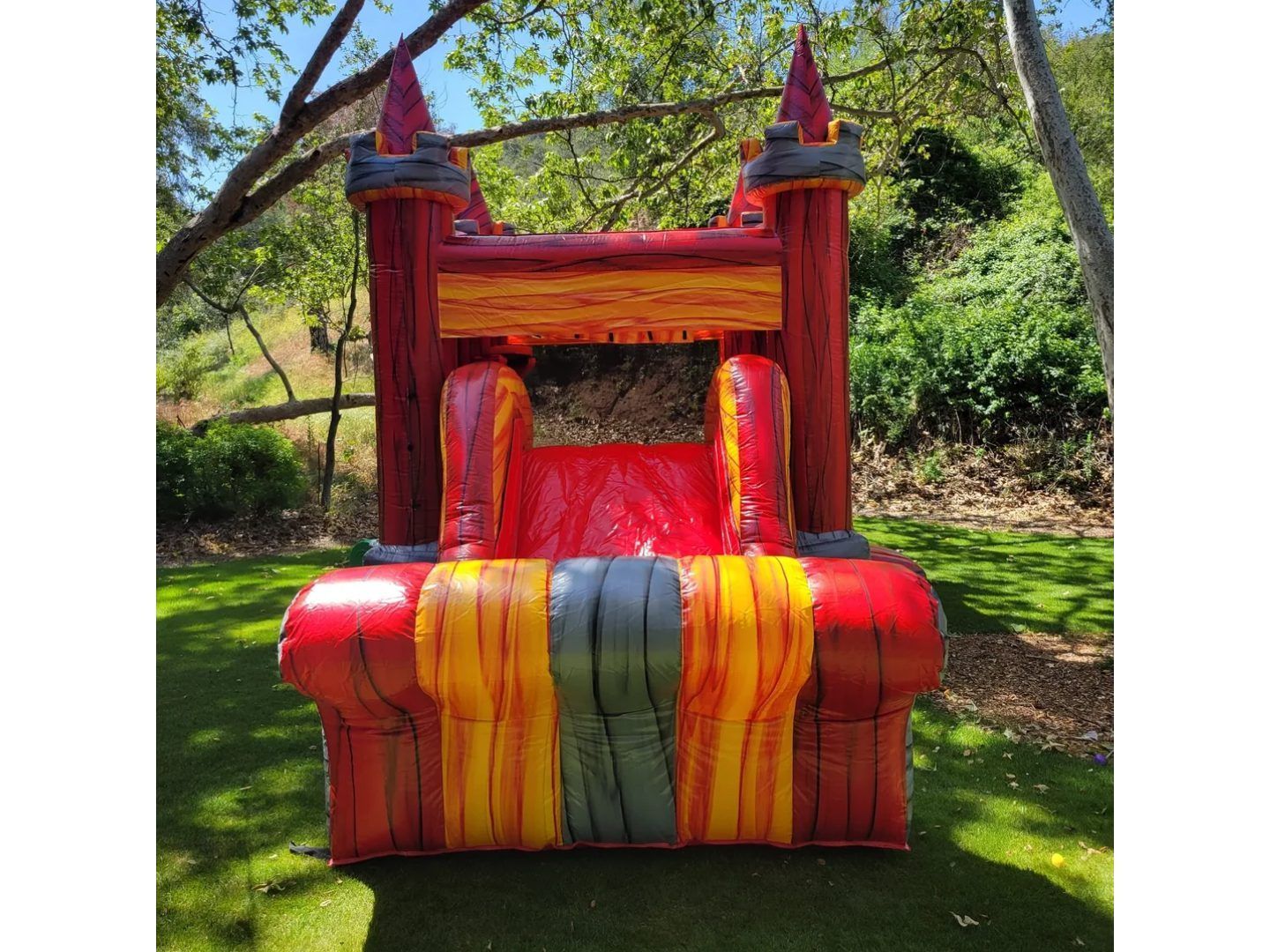 Colorful red, orange, and gray inflatable castle in a grassy park under trees