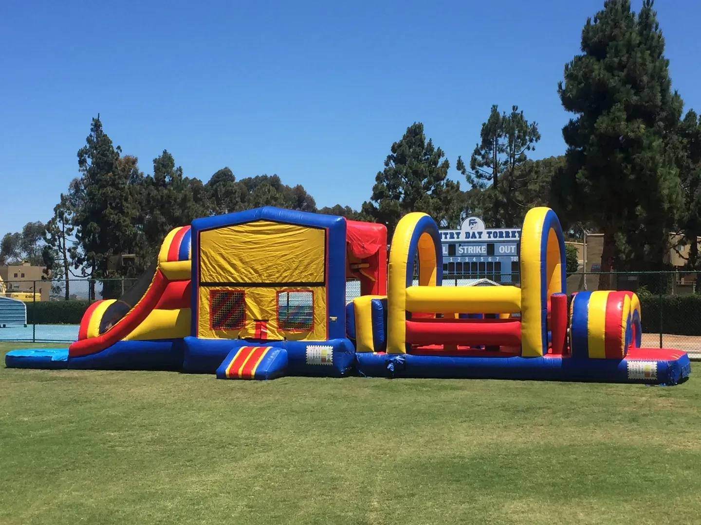 Colorful inflatable bounce house and slide on a grassy field under a sunny sky.