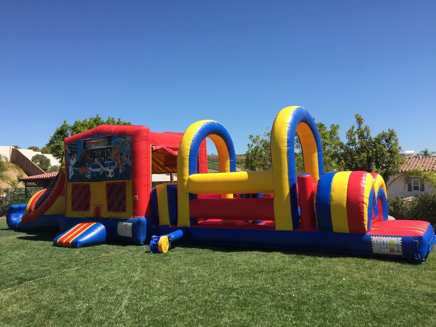 Colorful red, yellow, and blue inflatable bounce house on a grassy lawn under a clear blue sky
