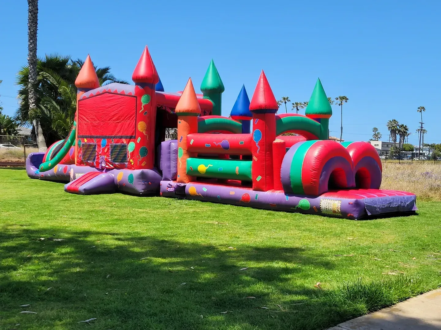 Colorful inflatable bounce house on a grassy field under a clear blue sky