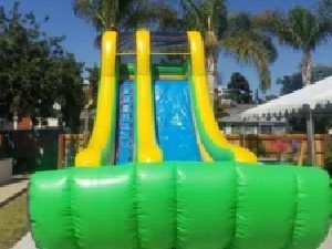 Inflatable green and yellow water slide under a sunny sky with palm trees nearby
