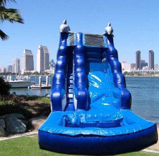 Blue inflatable water slide by a harbor with city skyline in the background