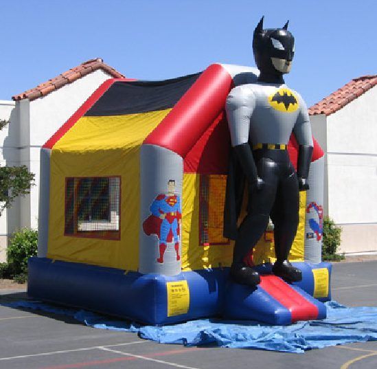 Batman-themed inflatable bounce house with a Superman graphic, red-yellow-black roof, and blue base outdoors